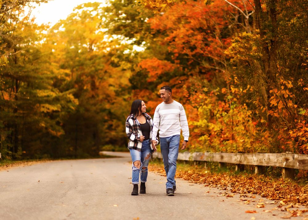 Couple walking hand in hand on tree-lined autumn road with golden foliage.
