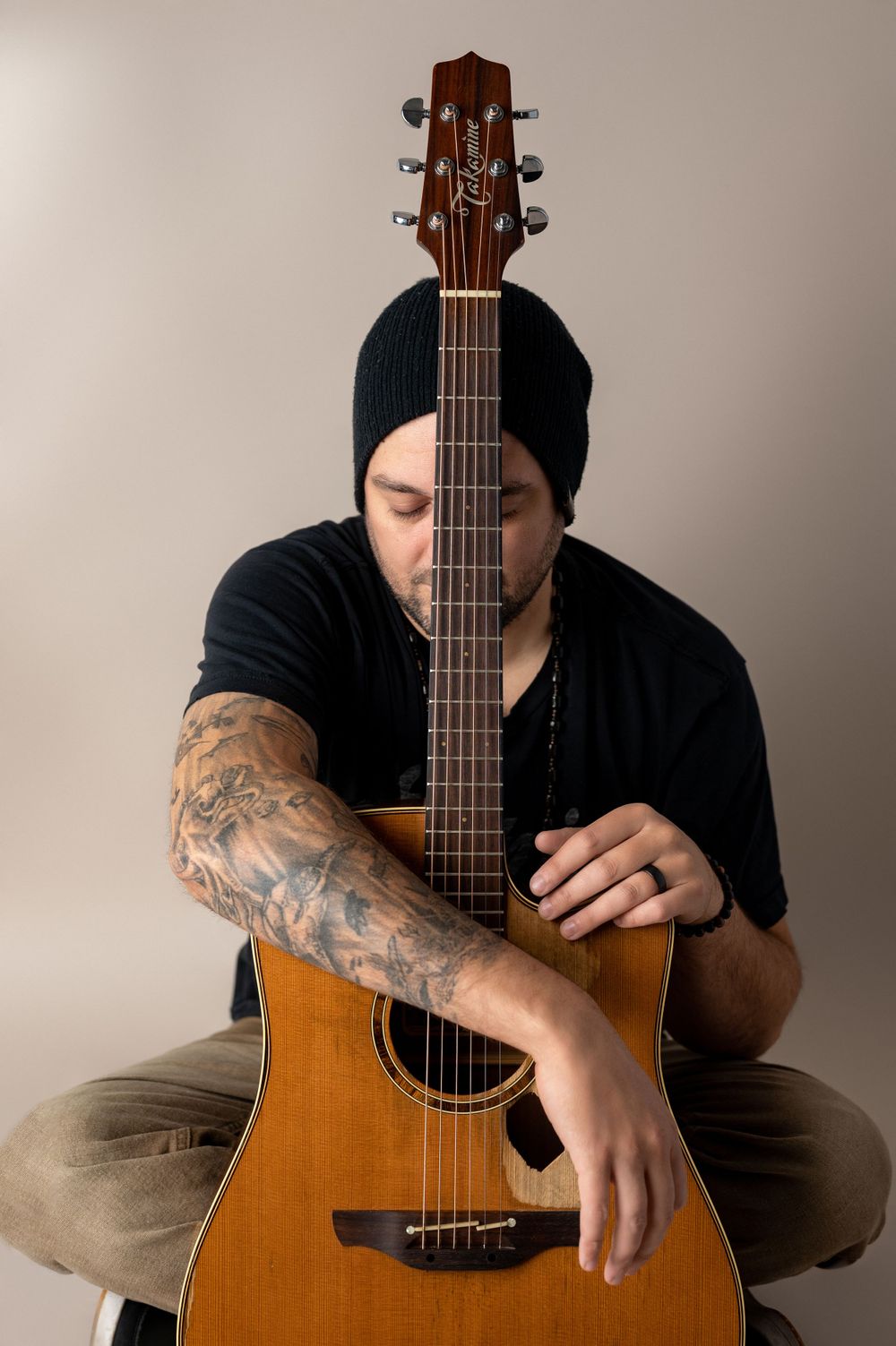 Creative portrait of guitarist with tattoos holding acoustic guitar in front of face.