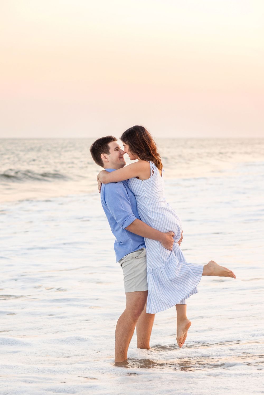 A couple embraces while standing in the ocean waves at sunset.