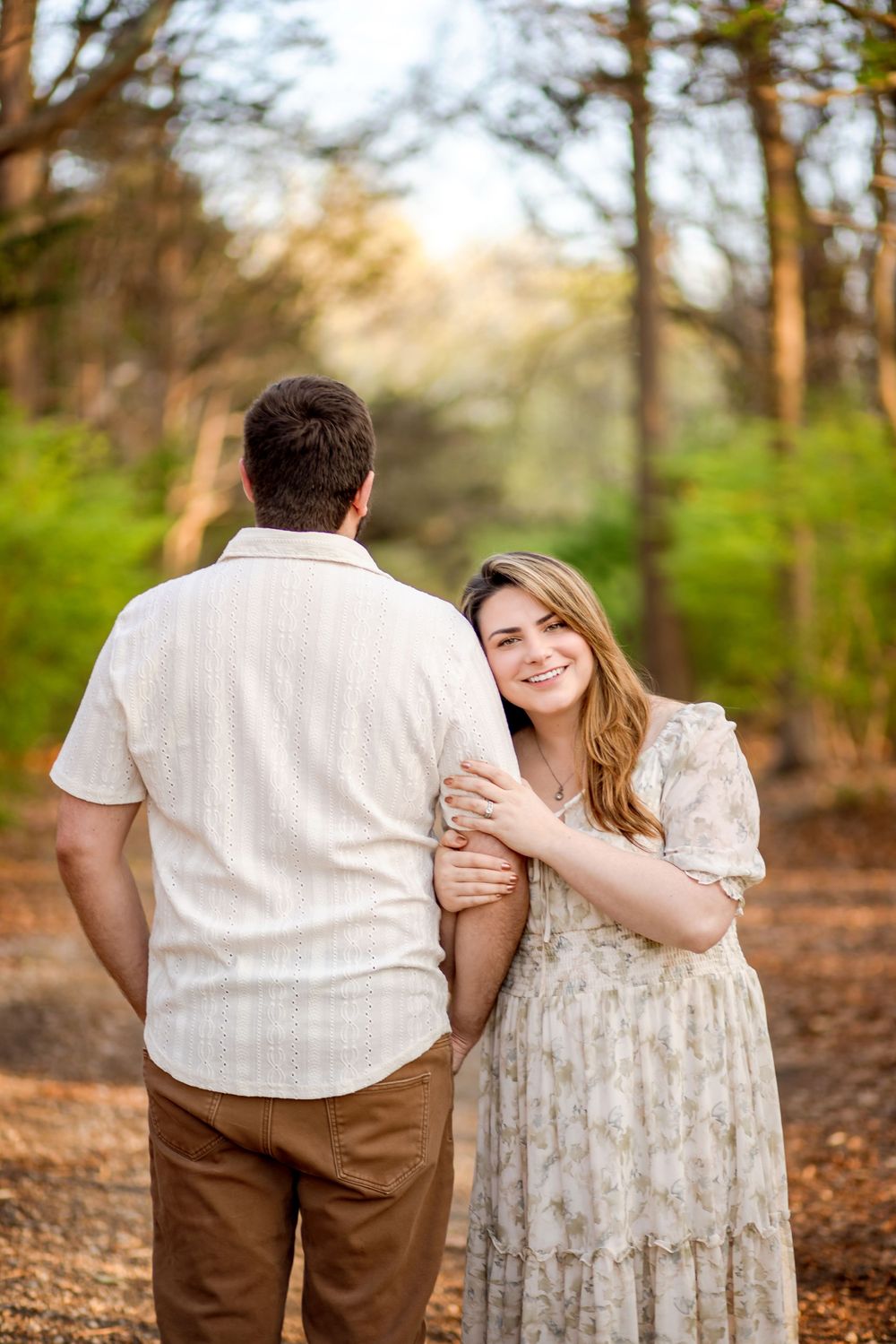 A couple shares a romantic moment on a wooded path during golden hour.