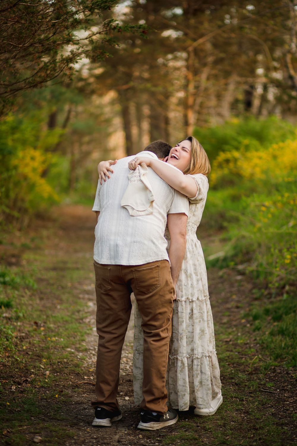 A couple shares an intimate moment while embracing on a forest path.