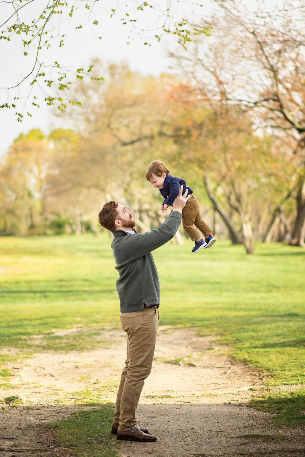 Playful moment in park as parent lifts child high in the air during autumn.