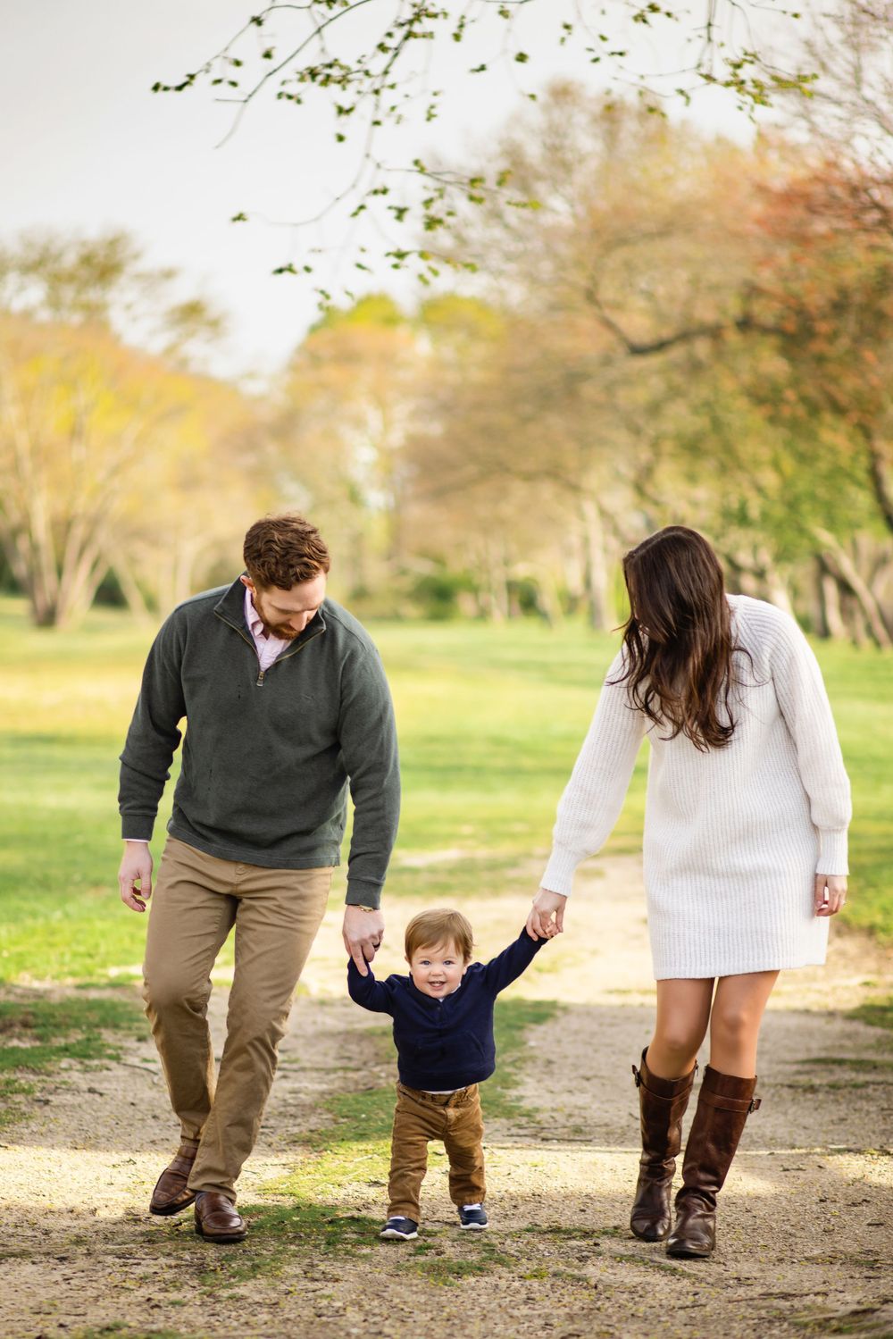Family walking together on autumn path holding hands with trees in background.