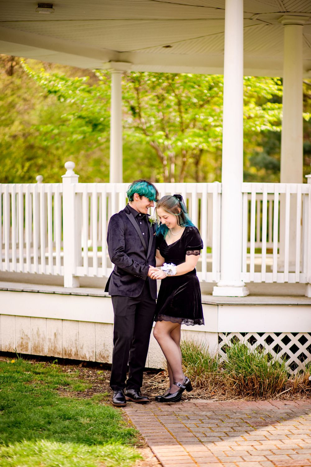 Couple in black formal wear sharing romantic moment on white gazebo porch.