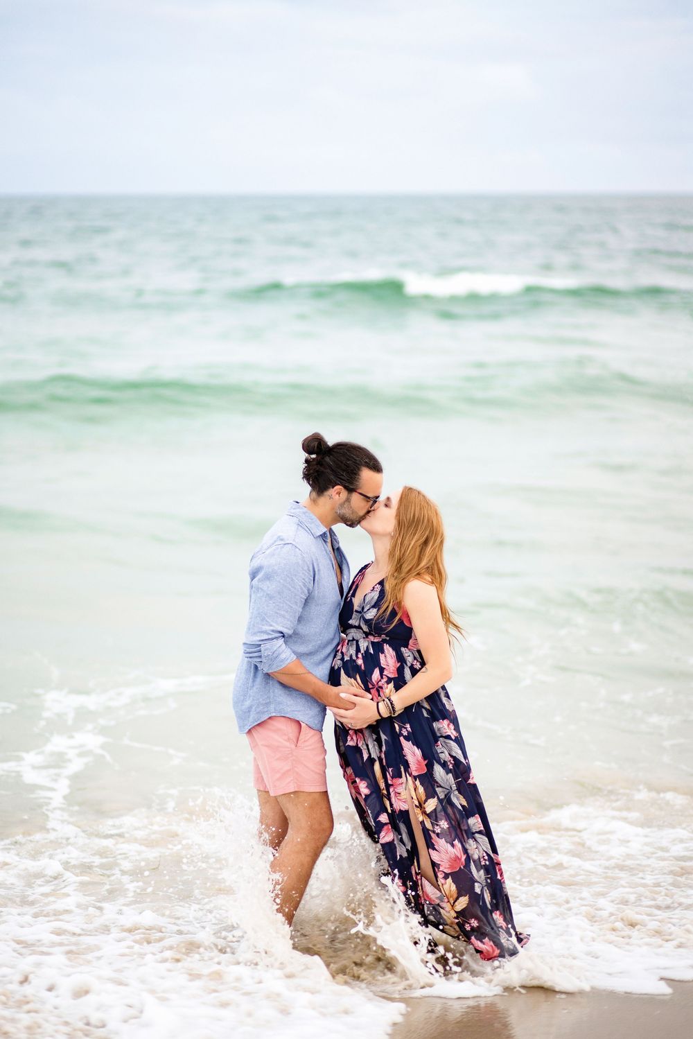A couple shares a romantic beach kiss sequence while standing in the ocean surf during golden hour.