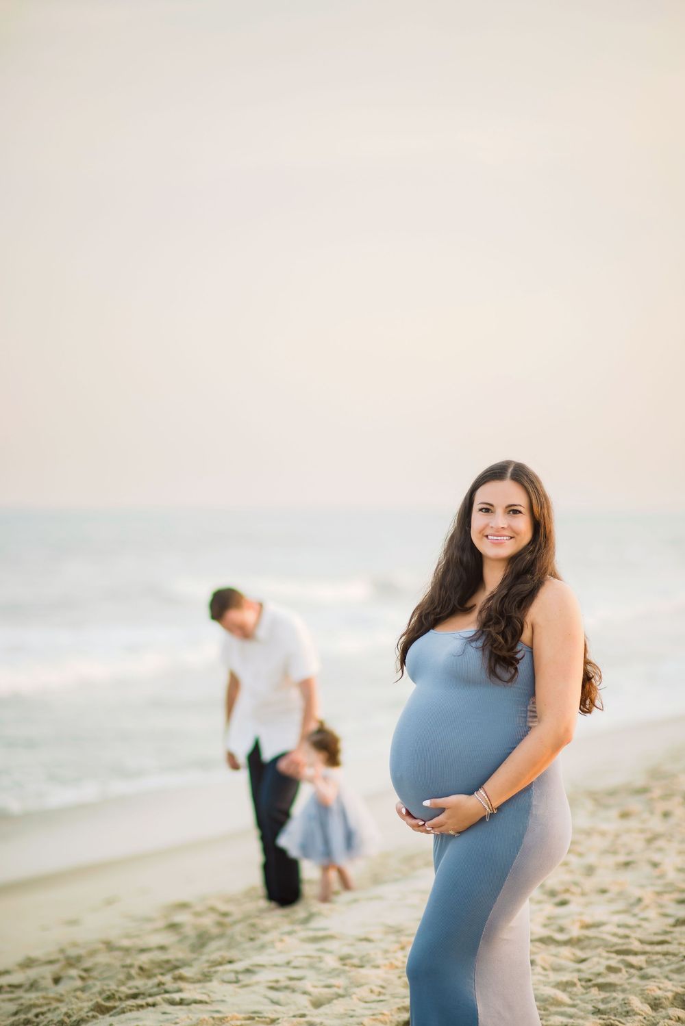 Expecting couple shares tender moments during their maternity photoshoot on a peaceful sandy beach at sunset.