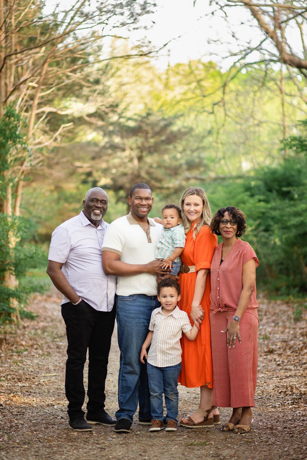 An extended family poses together on a tree-lined path during an outdoor photo session.