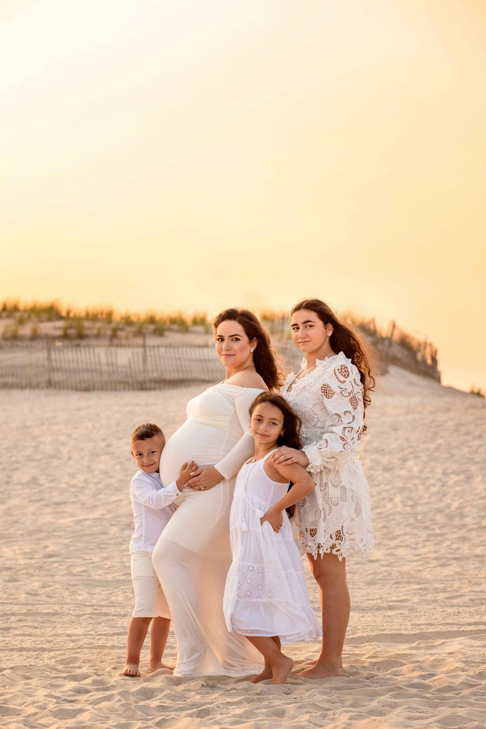 Beautiful sunset beach maternity photo showcasing family in white outfits on sandy shore.