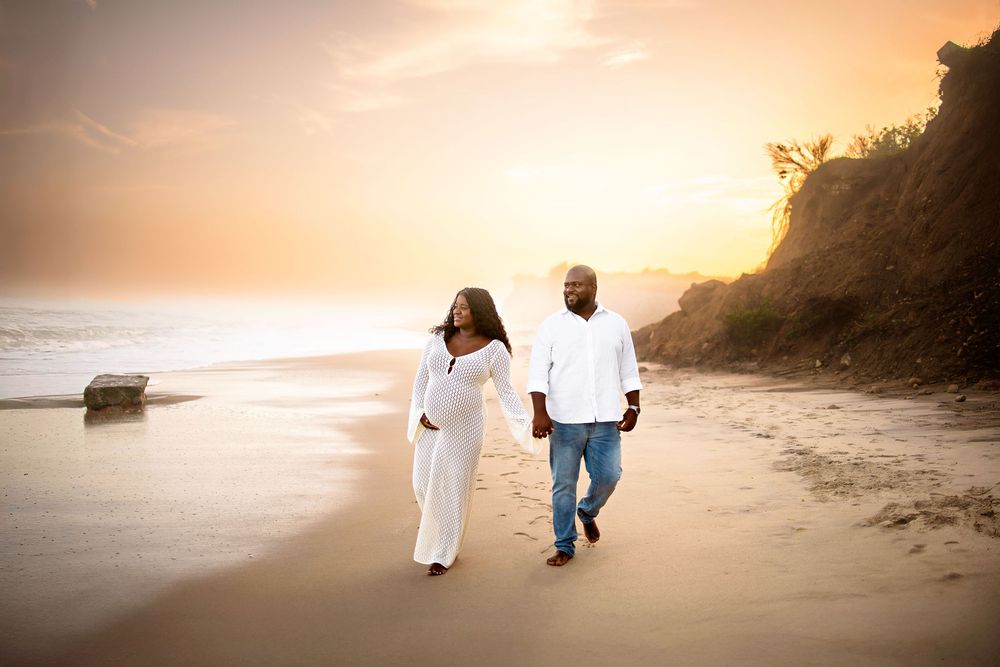 Two people walking together on a beach at sunset with golden light and cliffs in the background.