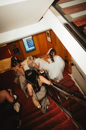 Bridesmaids in taupe dresses helping bride in white gown navigate staircase on cruise ship wedding.
