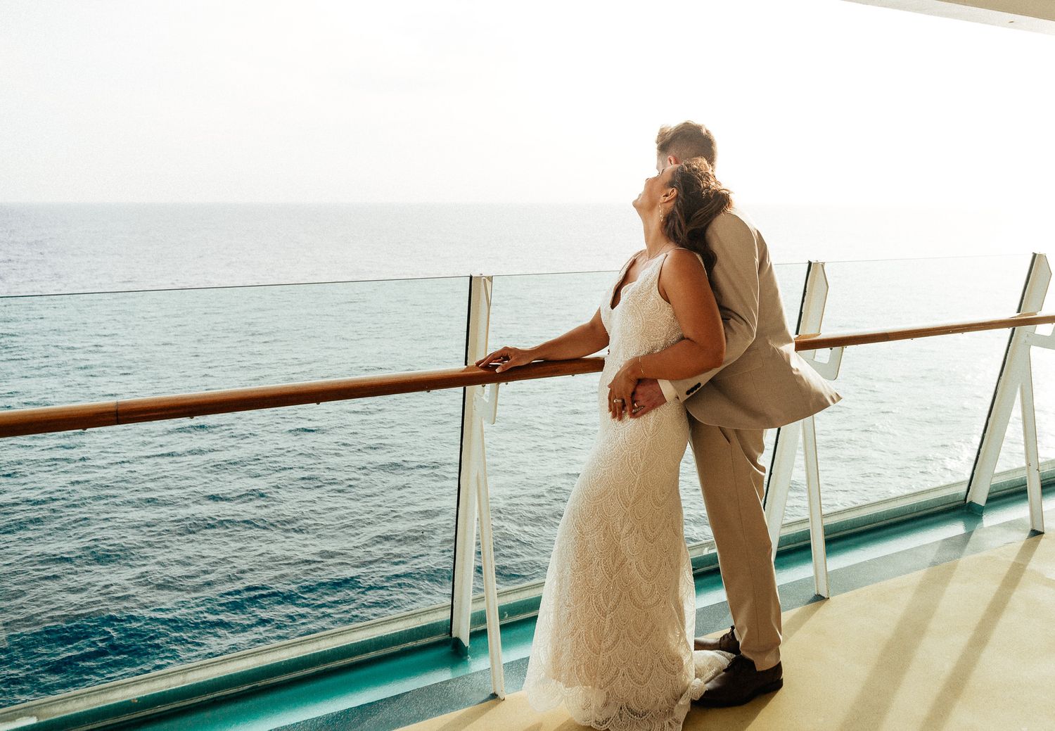 Bride and groom sharing a romantic kiss on a cruise ship balcony overlooking the calm blue ocean.