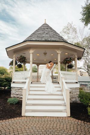 Bride and groom kissing on the steps of a white gazebo at an elegant outdoor wedding venue.