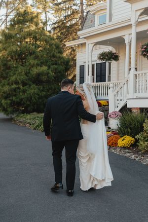 Bride and groom walking arm in arm toward a charming Victorian-style wedding venue surrounded by autumn flowers.