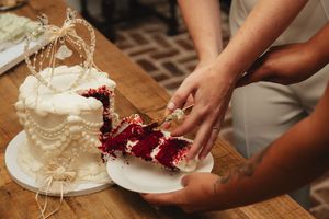 Couple cutting into a stunning white and red velvet wedding cake decorated with pearl accents.