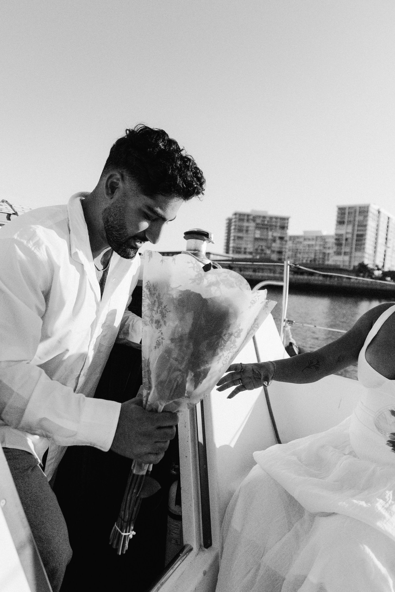 A couple share an intimate moment on a boat with city buildings visible in the background over the harbor.