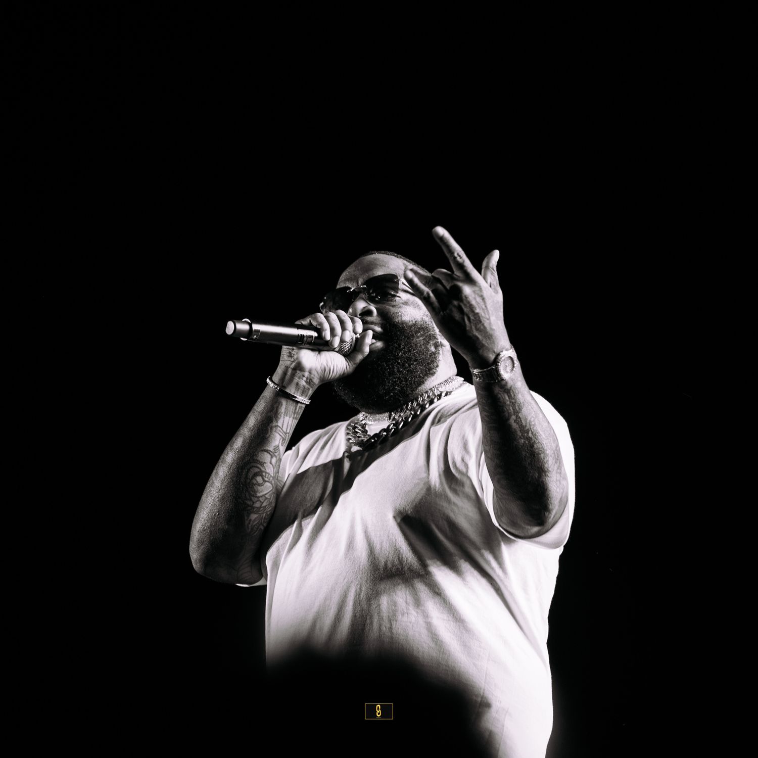 A performer in white clothing silhouetted against black background while holding microphone.