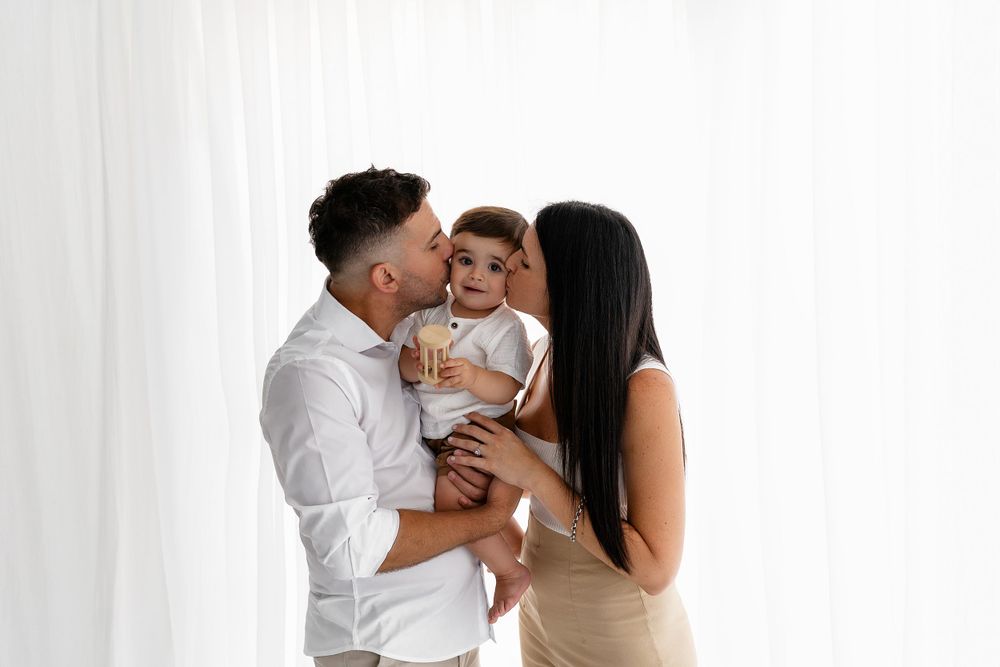 A loving family in white standing together against a white backdrop, sharing sweet moments with their baby.