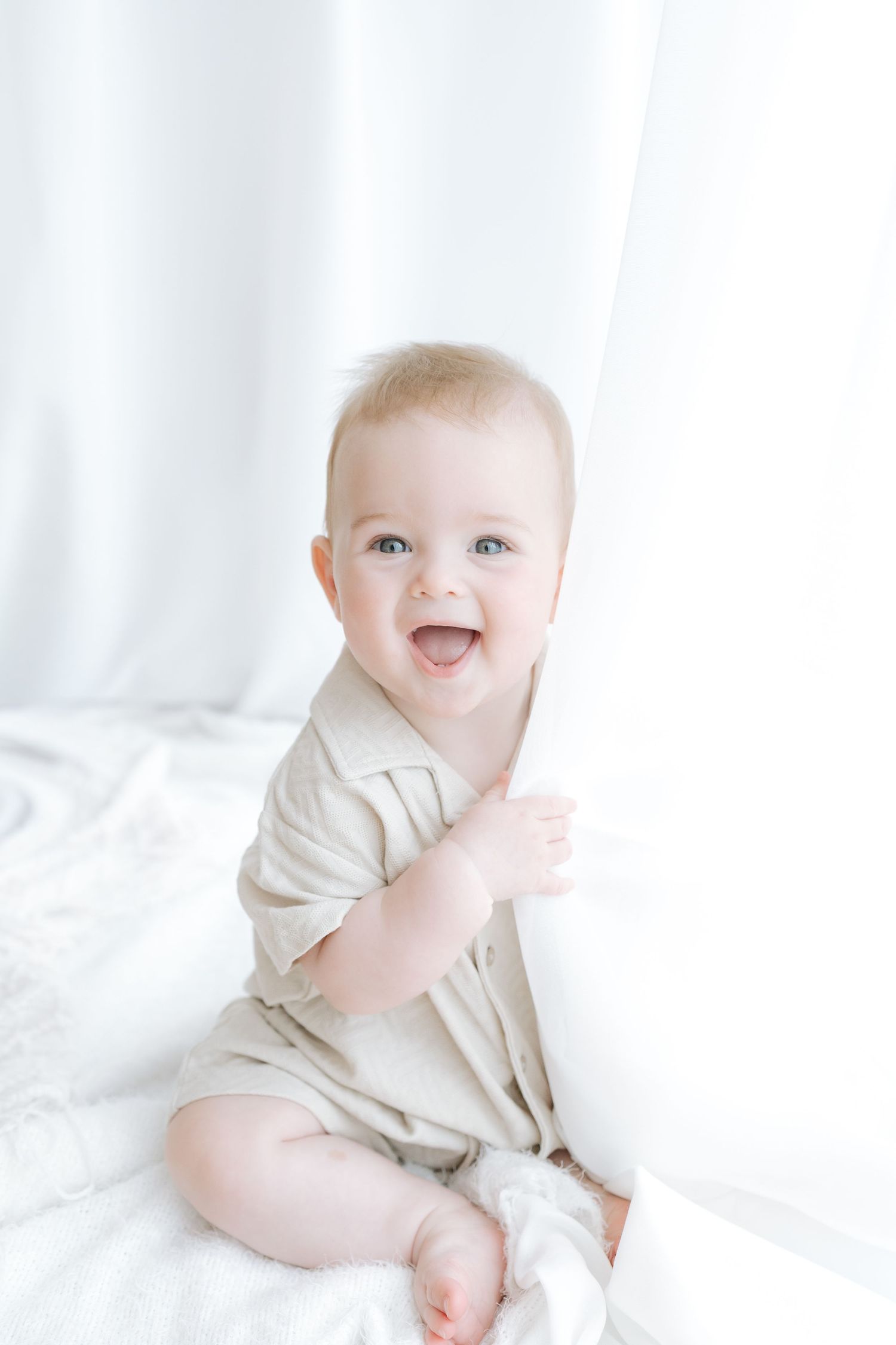 Baby in lace outfit crawls on white bedding with pink flowers in background.