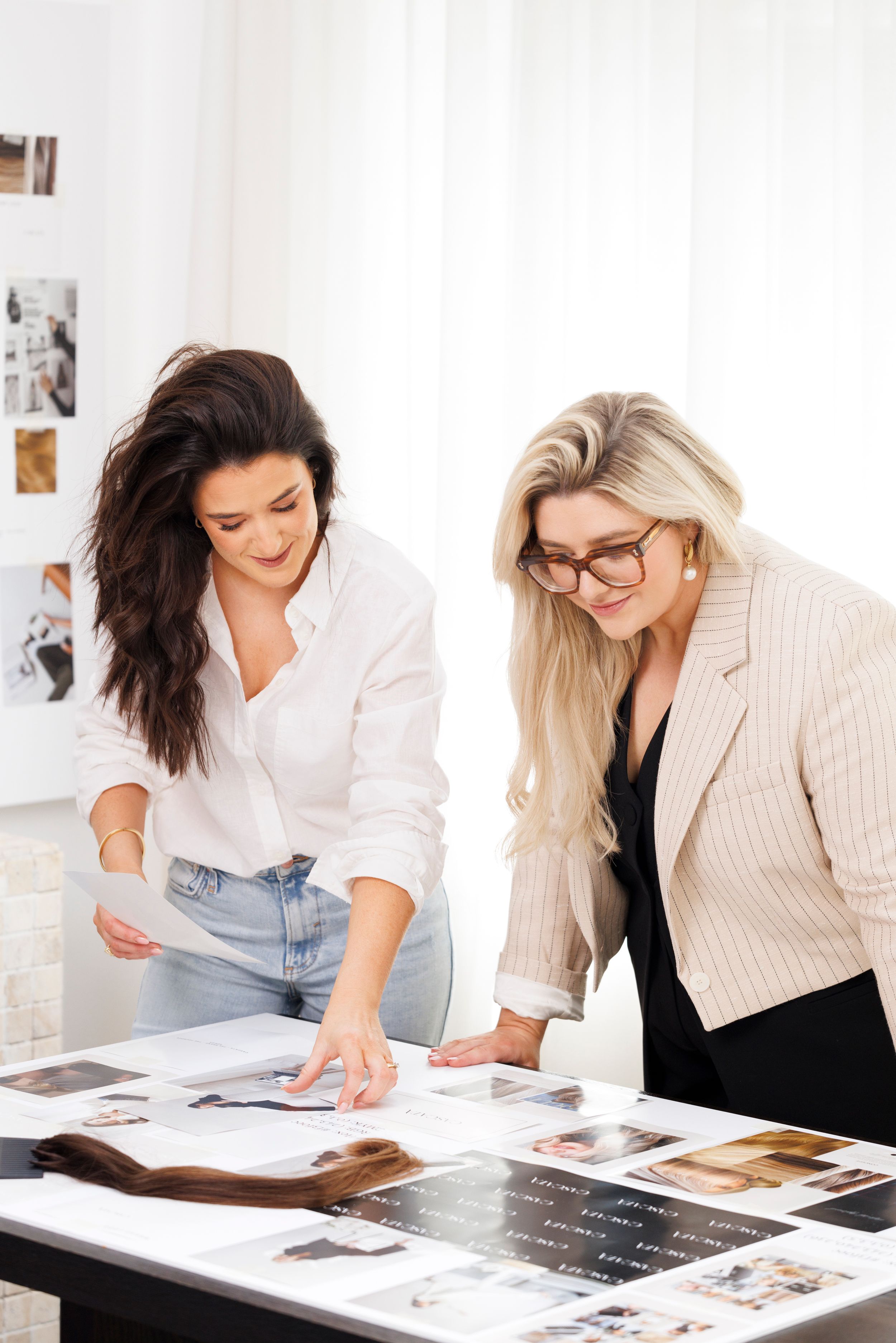 Two professionals reviewing design layouts and photo prints spread across a table in a bright studio setting. Personal Branding Photography.