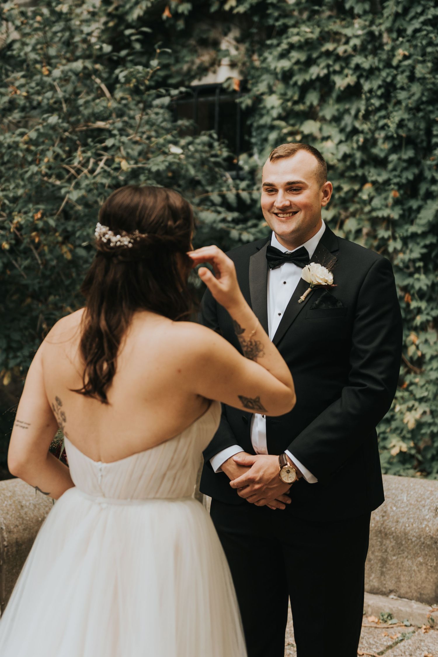 A romantic wedding first look moment between newlyweds outdoors with ivy-covered walls in the background.