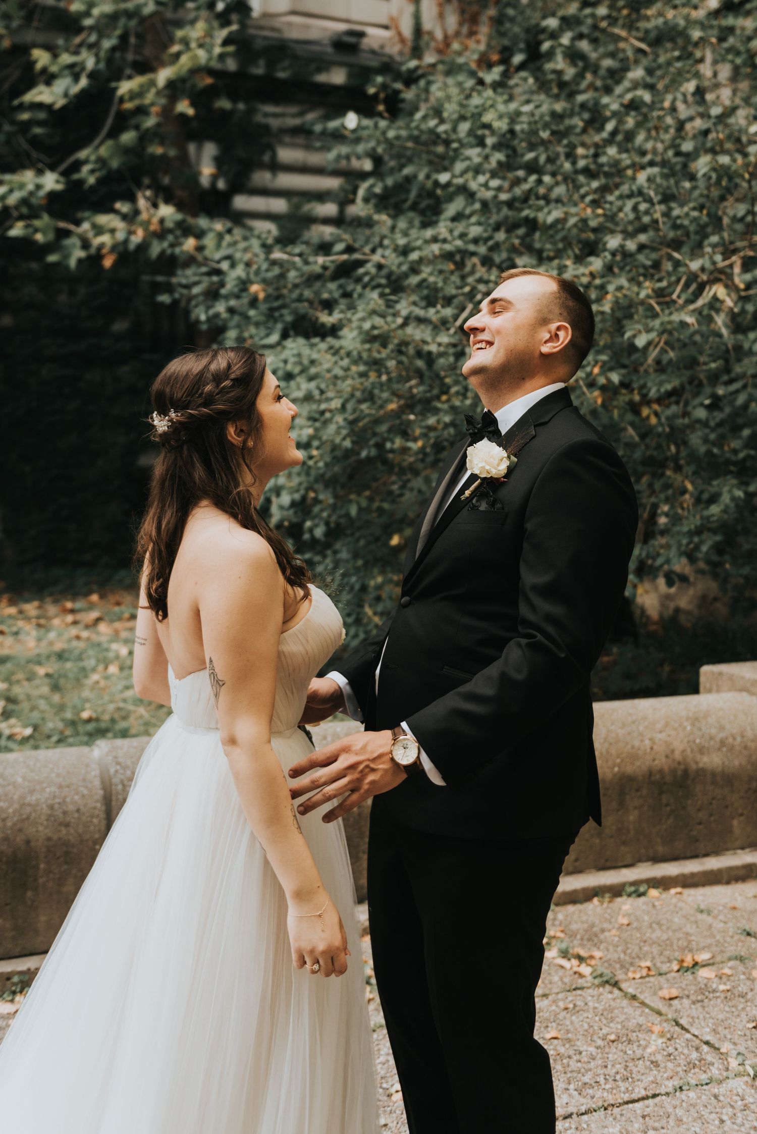 Candid wedding moment showing a joyful couple laughing together in front of lush greenery.