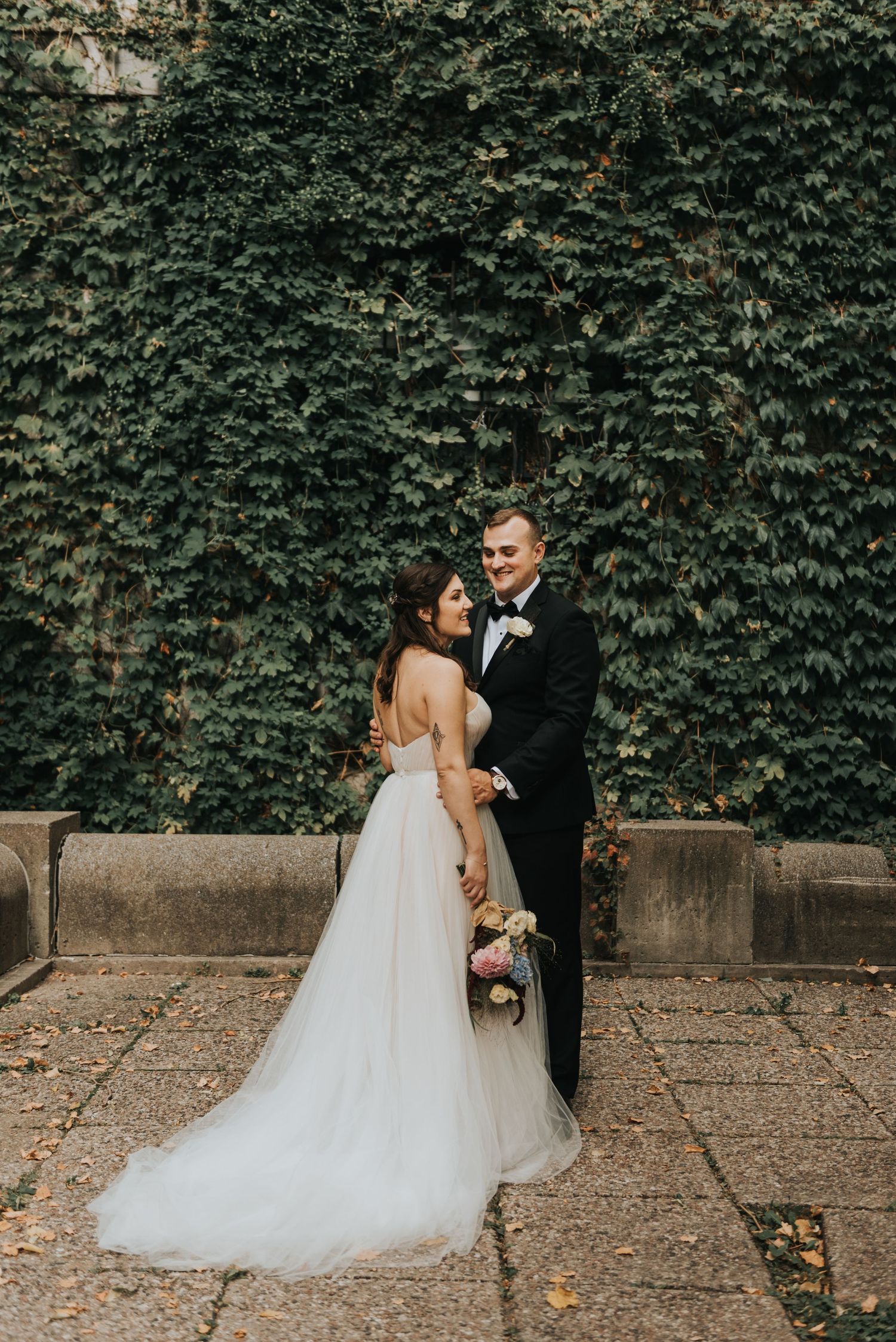 Elegant wedding portrait of a couple standing against an ivy-covered wall with the bride in a flowing white dress.