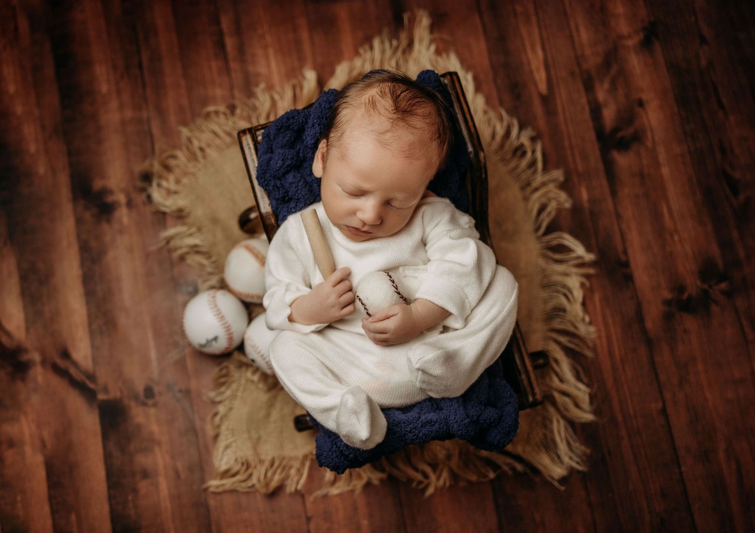 Overhead view of sleeping baby in white onesie laying on soft blue and beige textured blankets on wooden floor.