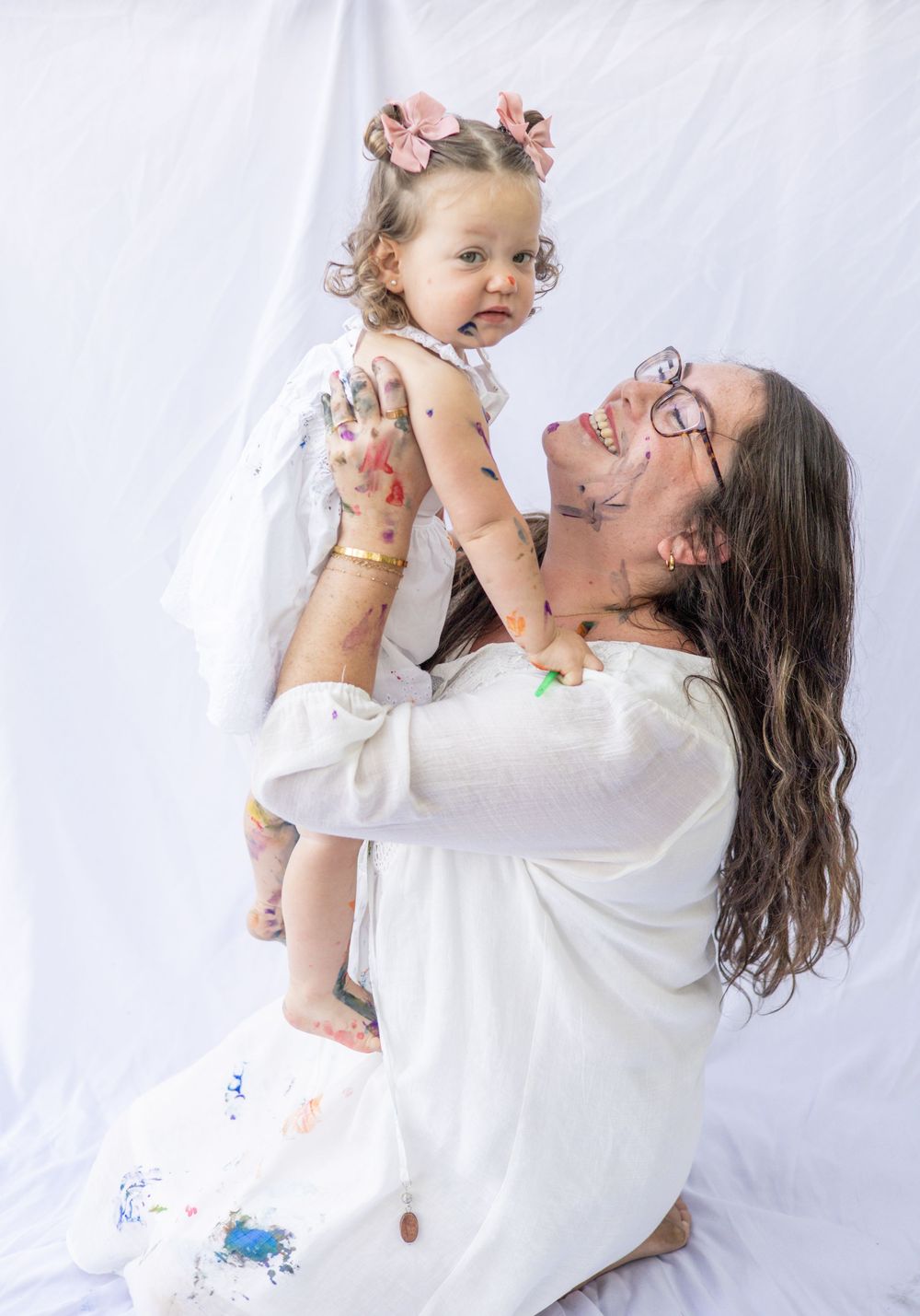 A joyful moment captured against a white backdrop showing playful interaction in matching white outfits with paint stains.