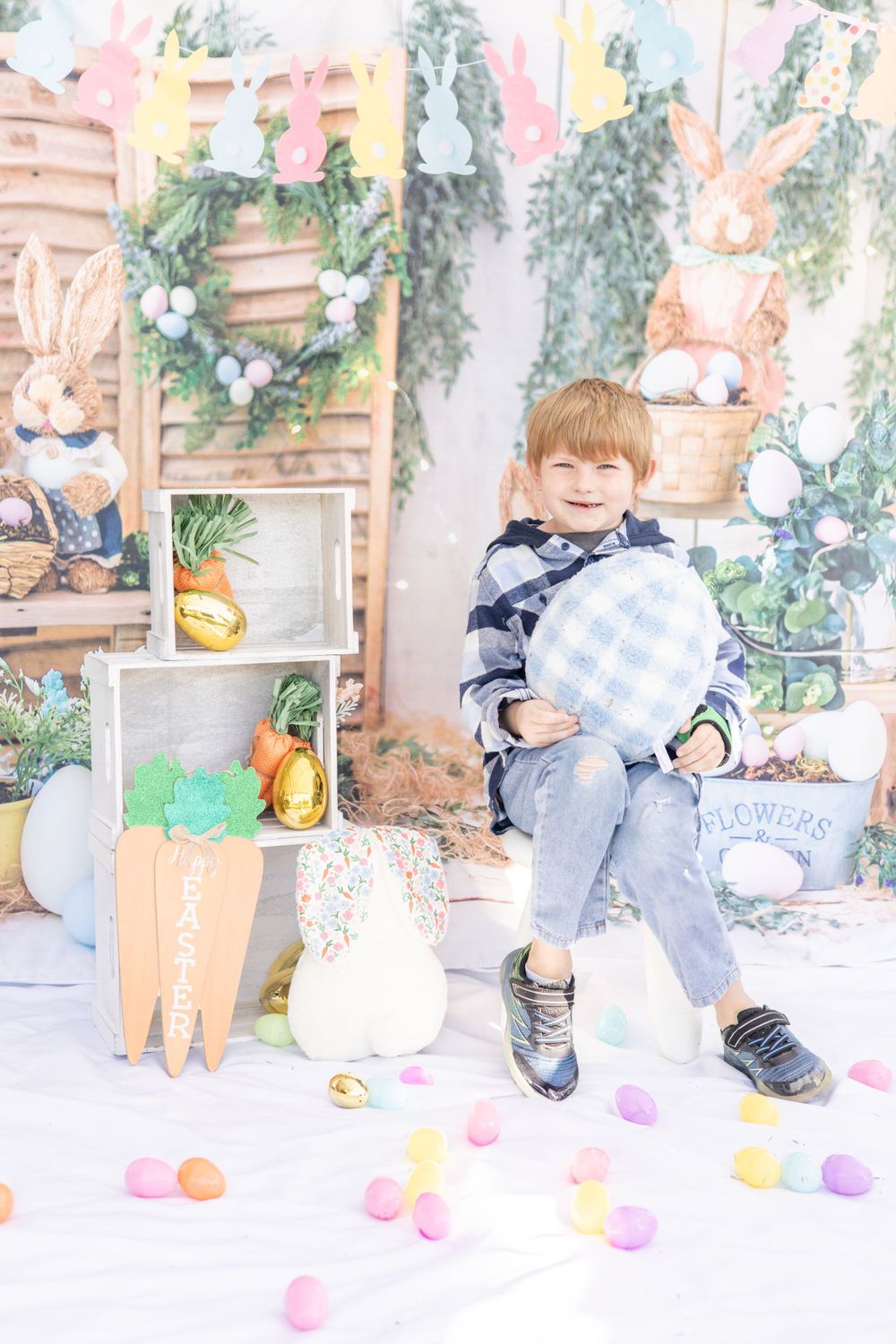 Festive Easter photo setup with pastel decorations, colorful eggs scattered on floor, wreath and wooden backdrop.