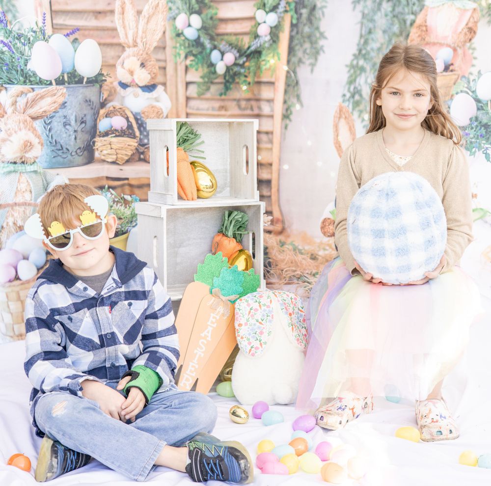 Children celebrate Easter surrounded by colorful eggs, plush bunnies, and rustic farmhouse decor at a spring-themed setup.