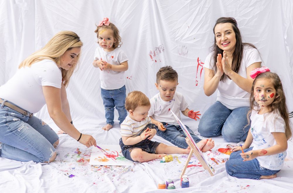 A family group sitting on a white sheet enjoys creative painting activities together during an art session at home.