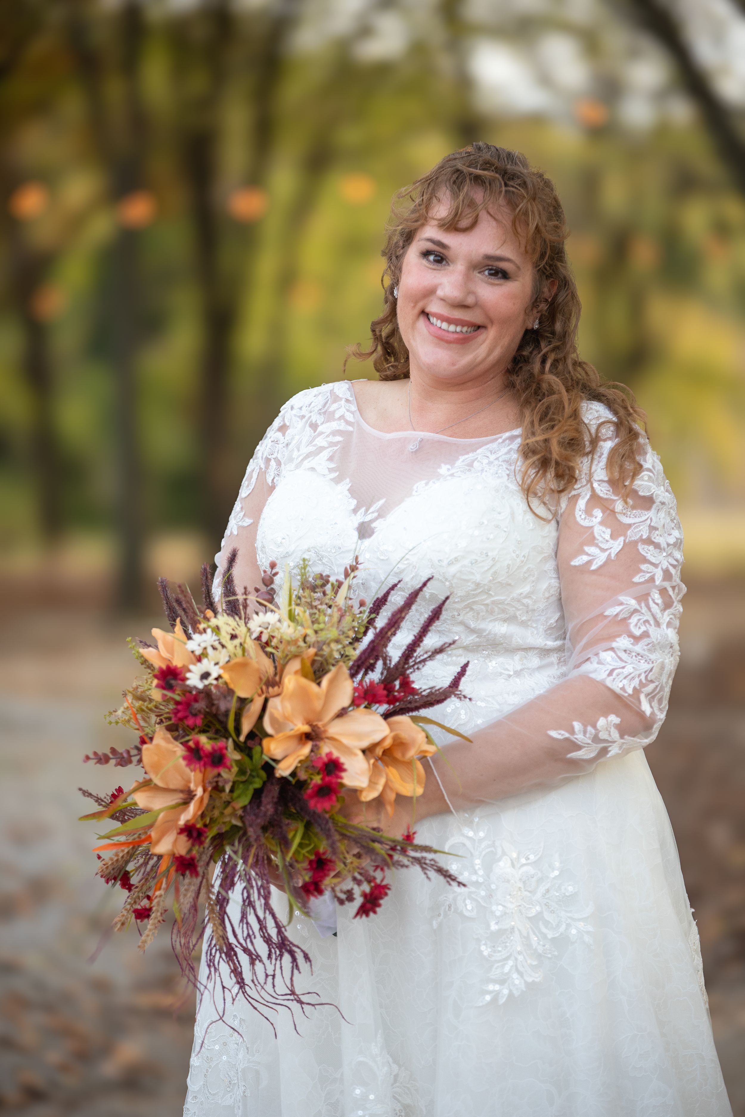 A bride holds a vibrant fall bouquet featuring orange and burgundy flowers.