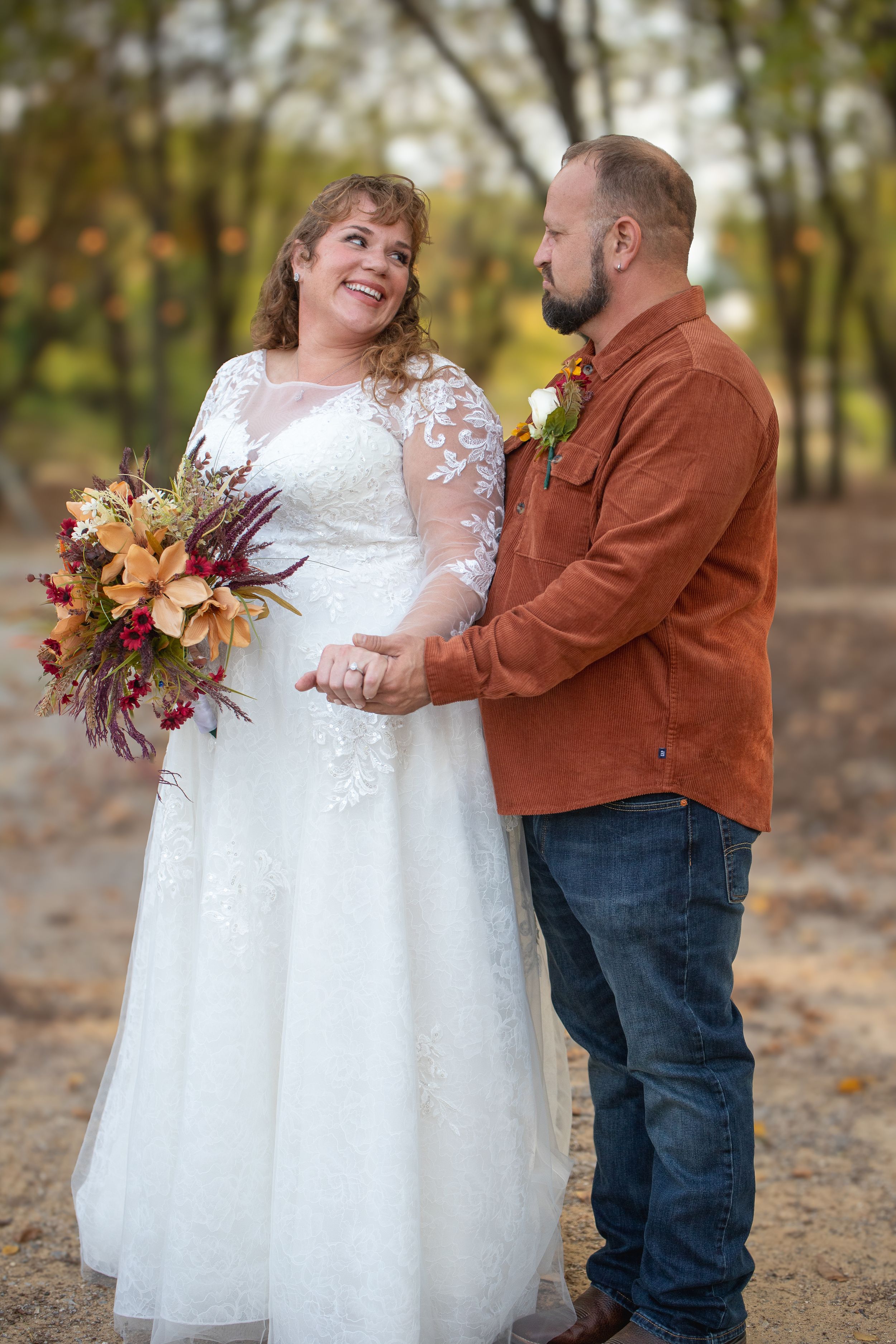A couple shares a romantic moment in autumn leaves wearing white dress and brown jacket.