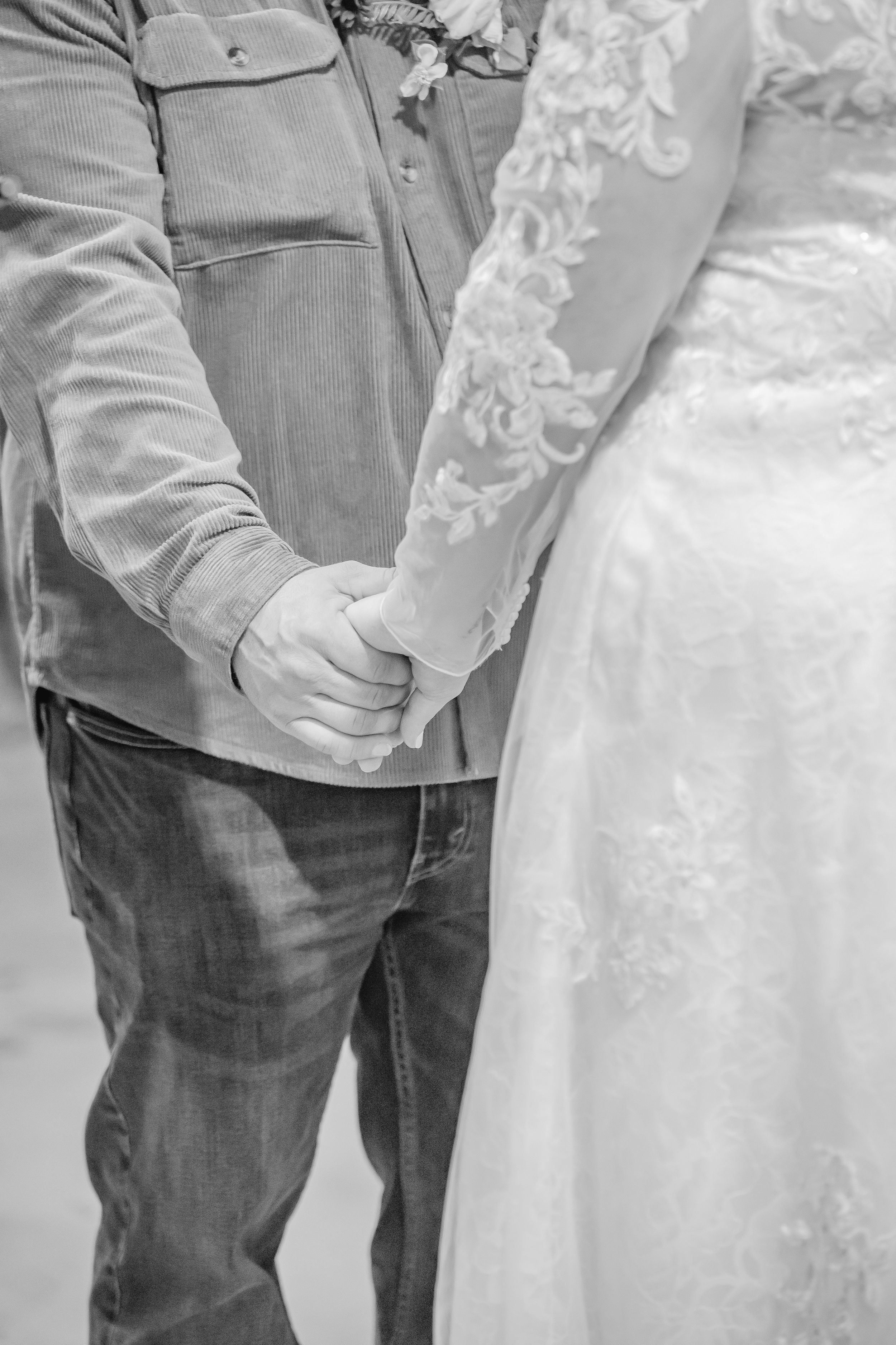 Close-up of a couple's formal attire showing white lace dress and casual jacket.