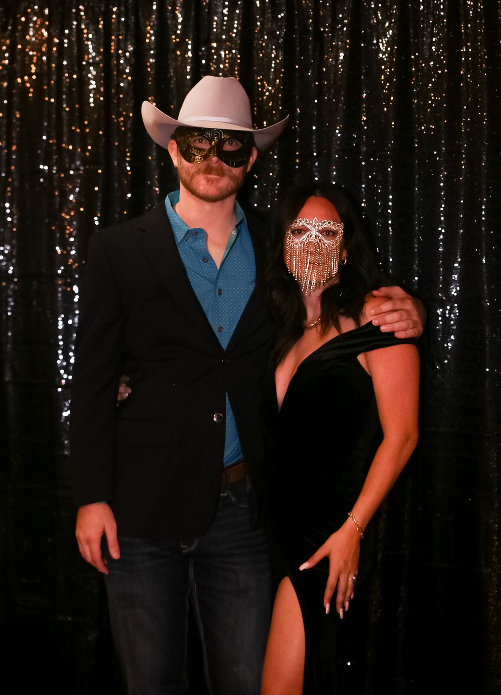 Formal party guests pose in western attire with masks against a shimmering backdrop.
