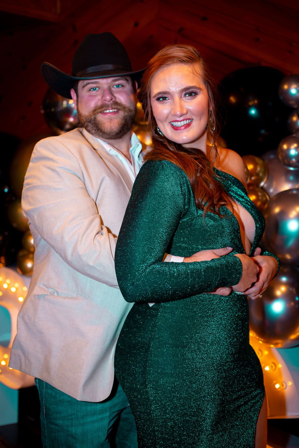 A couple embraces while dancing, with one wearing a green sparkly dress and the other in a light colored jacket.
