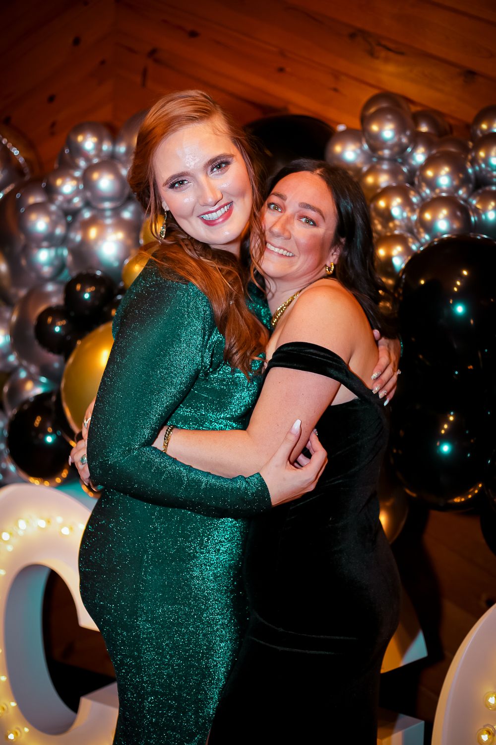 People embracing at a party with a sparkly green dress and silver balloon decorations.