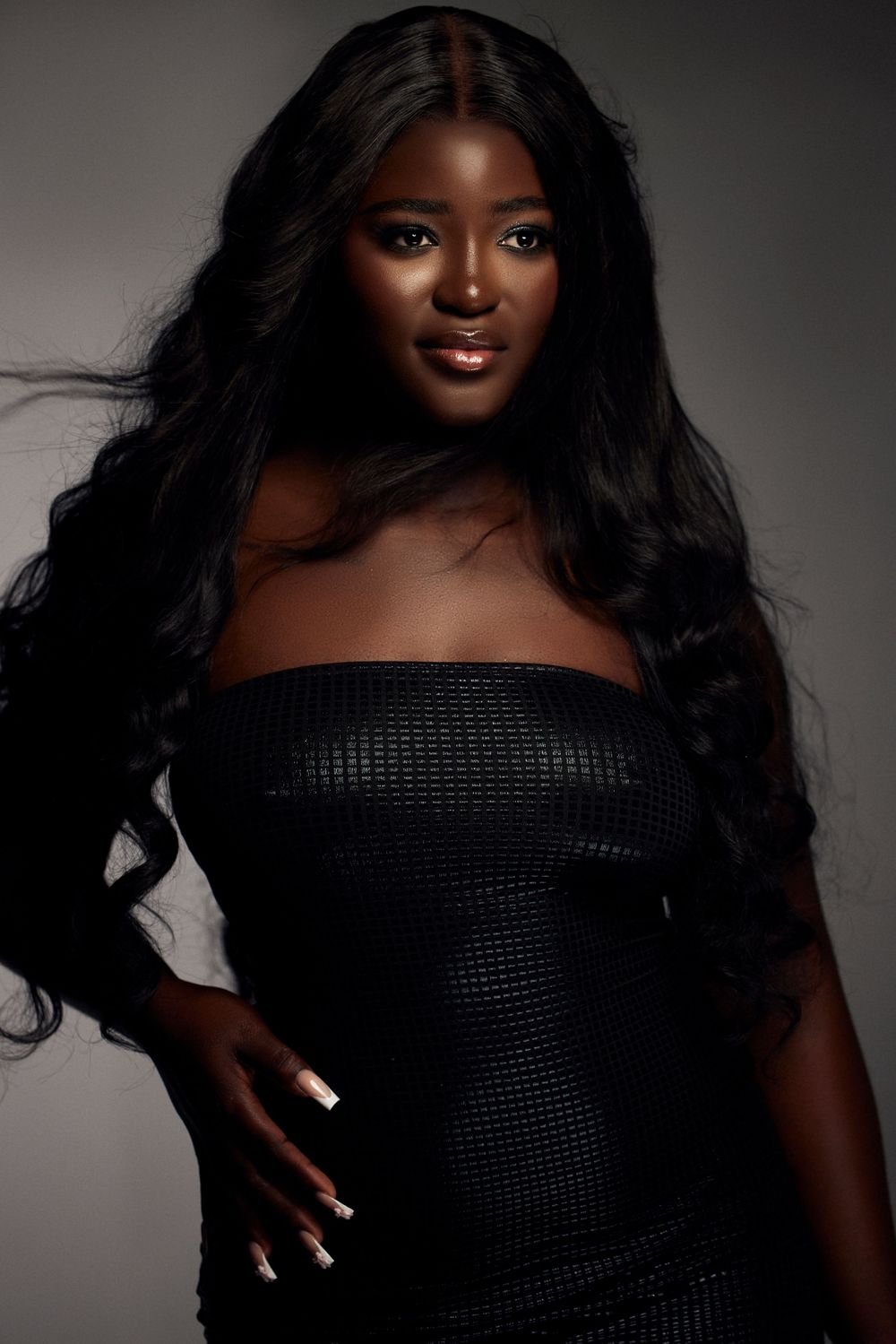 Dramatic portrait series in black dress with off-shoulder neckline against grey backdrop.