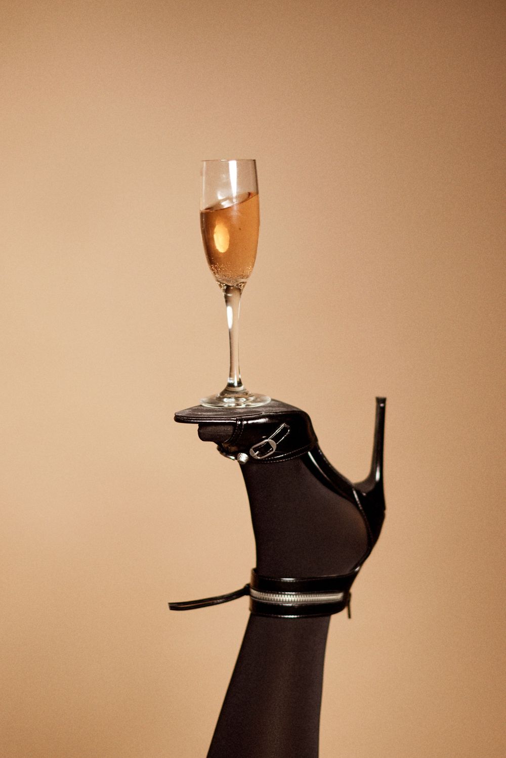 Wine glass balanced on black dress form mannequin against warm beige background.
