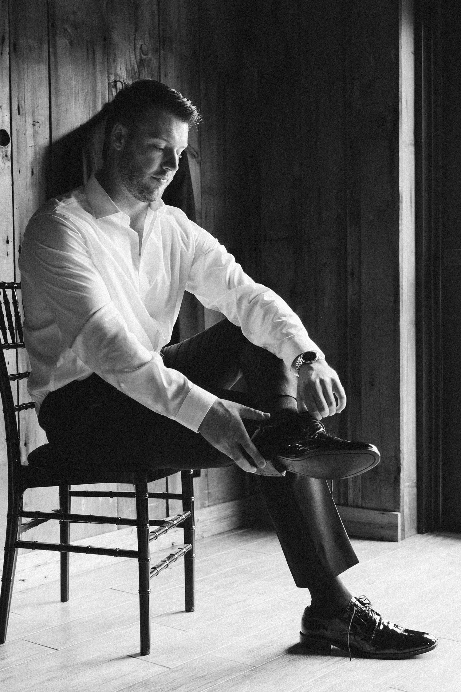 Black and white portrait of person putting on dress shoes in wooden interior.