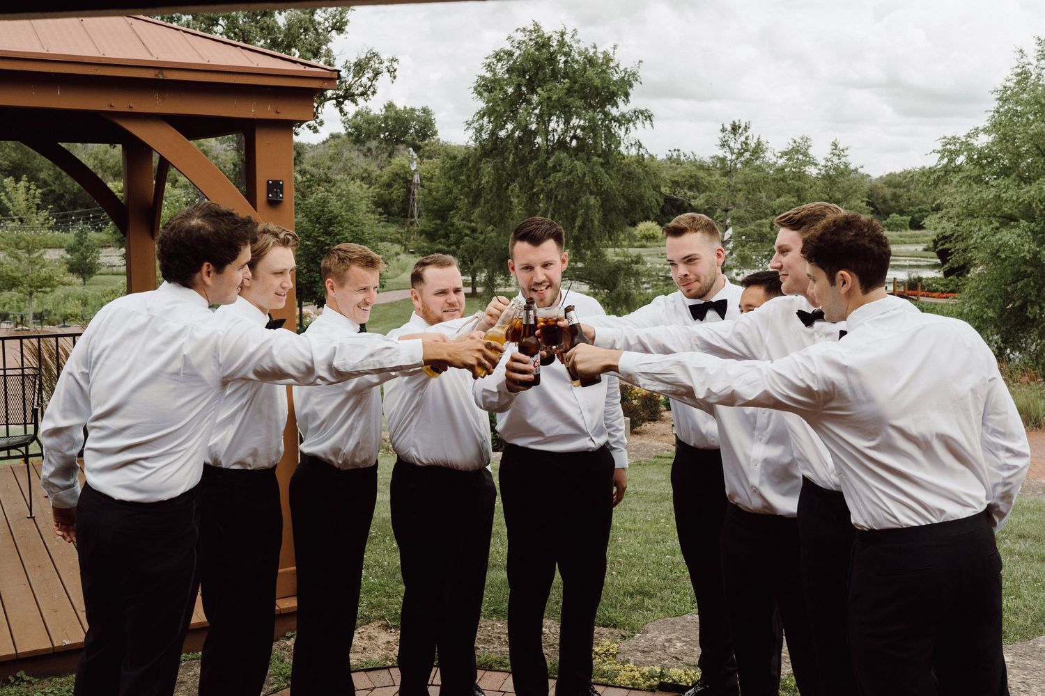 Groomsmen in white shirts and suspenders pose in a fun line formation outdoors.