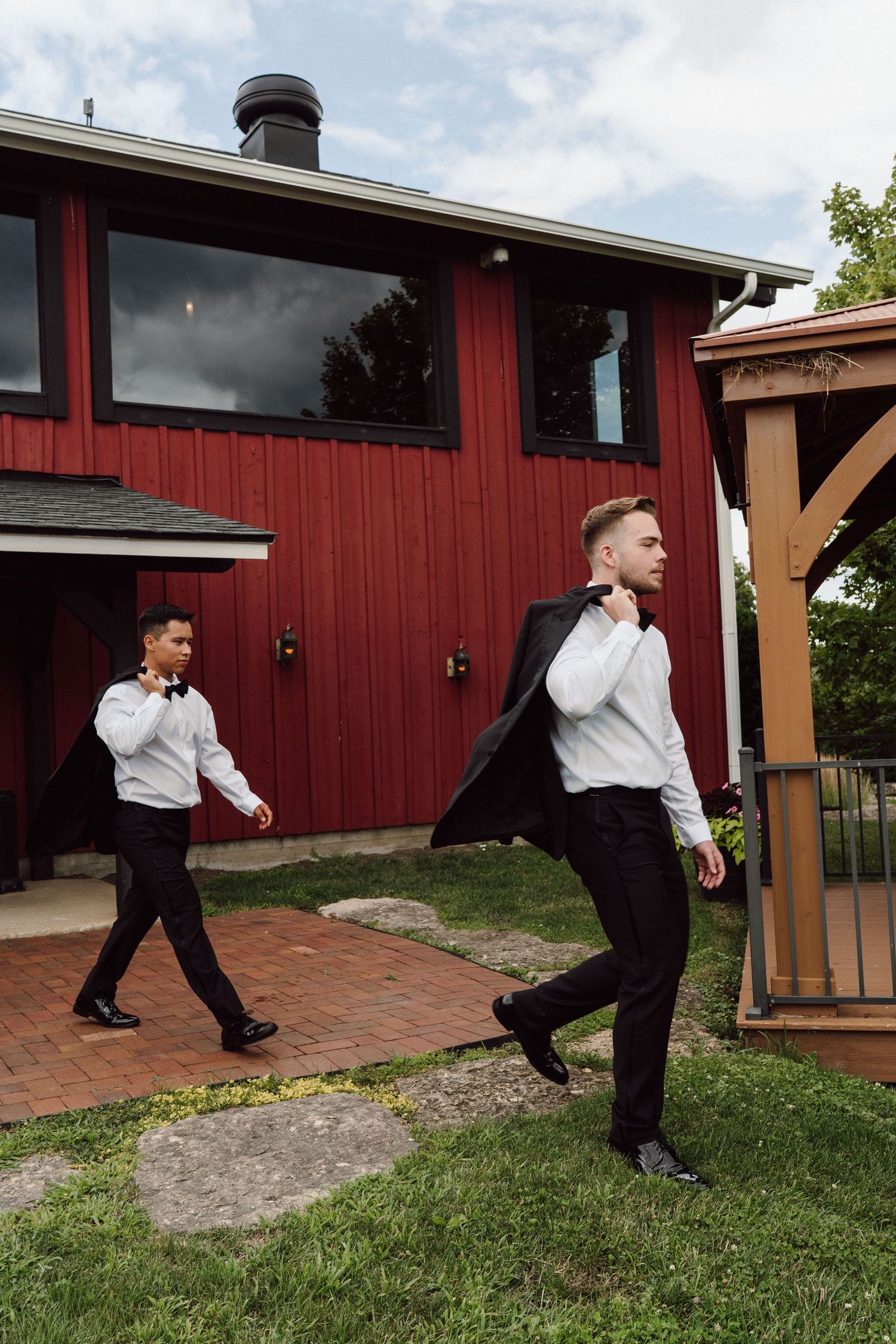 Groomsmen perform synchronized dance moves outside a red barn building.