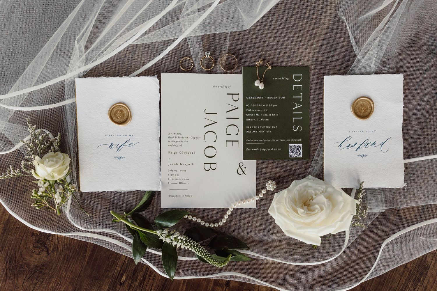 Wedding stationery and details including invitations, rings, and floral elements on a dark wooden surface.