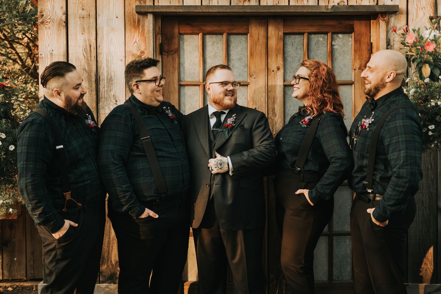 A group of people in black formal attire stand together in front of a rustic wooden door.