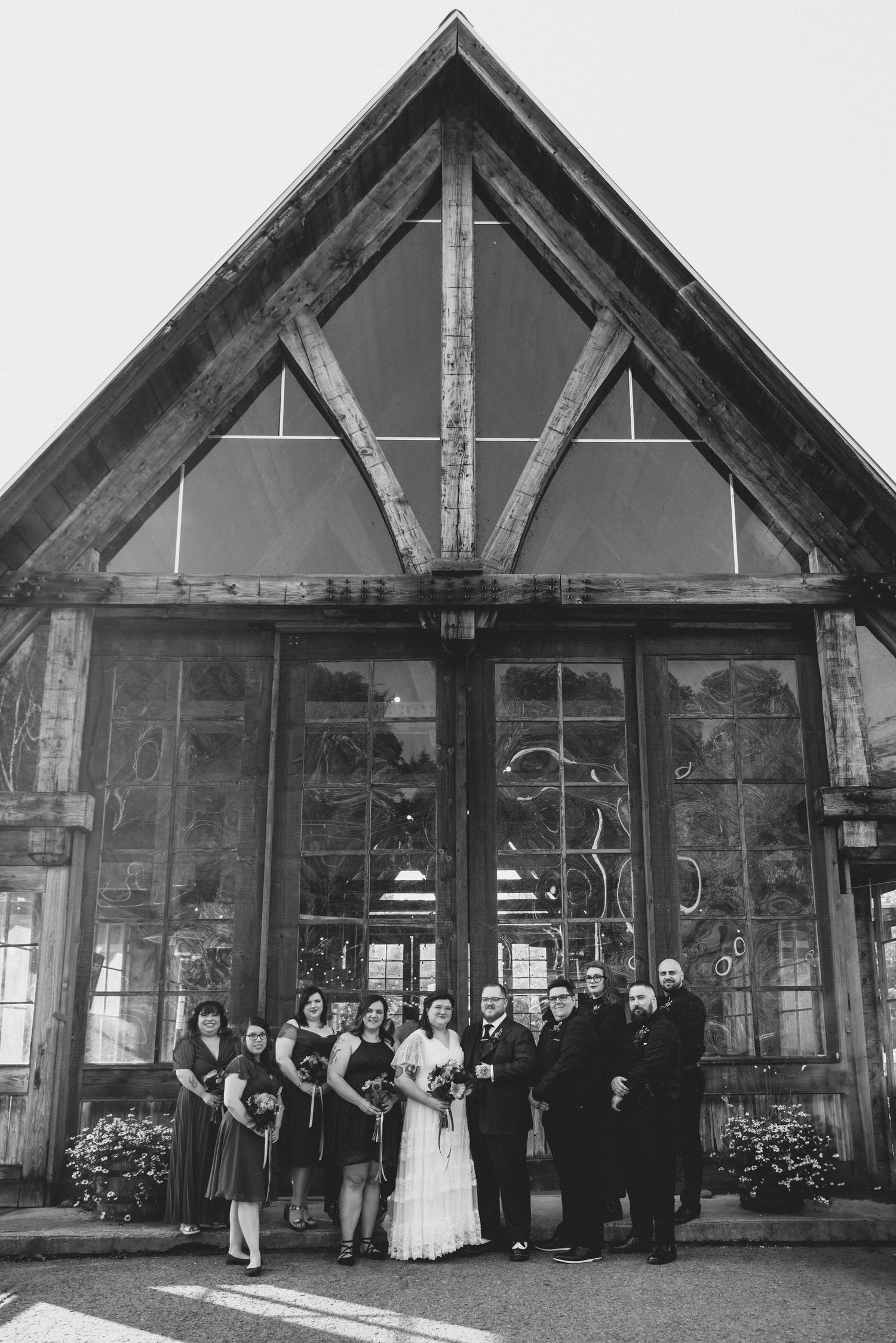 Wedding party poses in front of rustic wood and glass chapel entrance in black and white photograph.