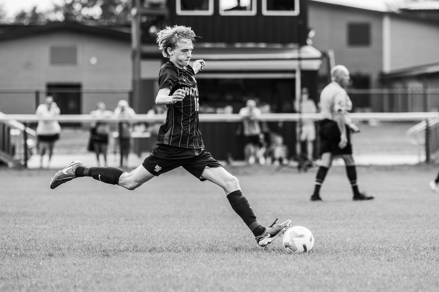 Two soccer players leap into the air competing for possession during a black and white match on a sports field.
