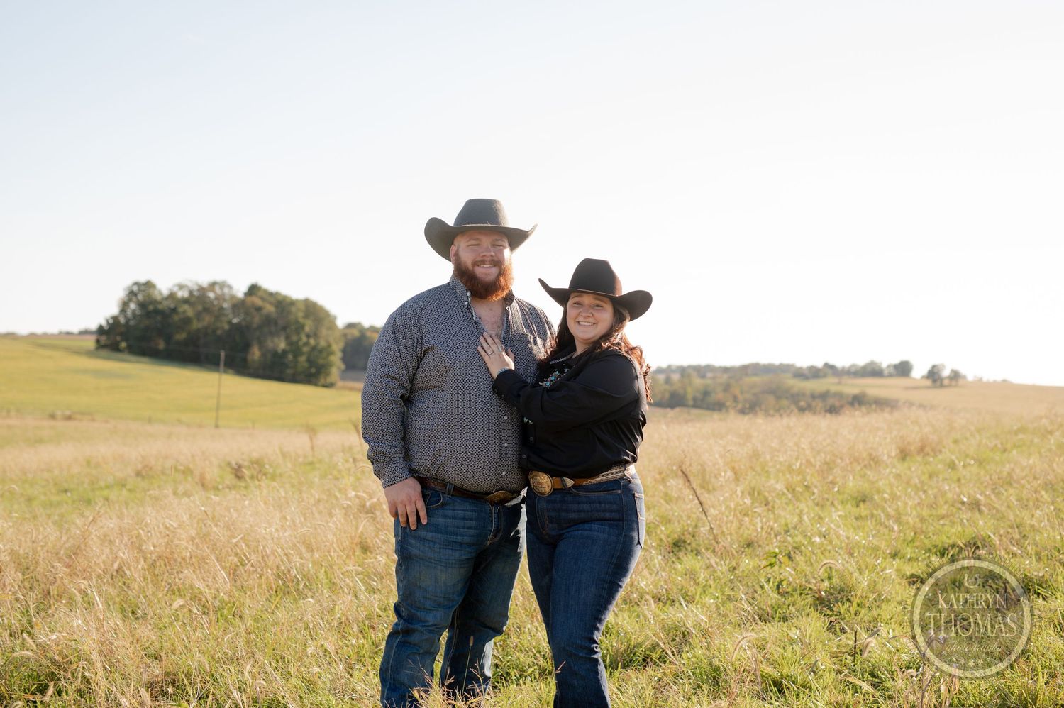 Western couple in cowboy hats embrace in sunny prairie field.