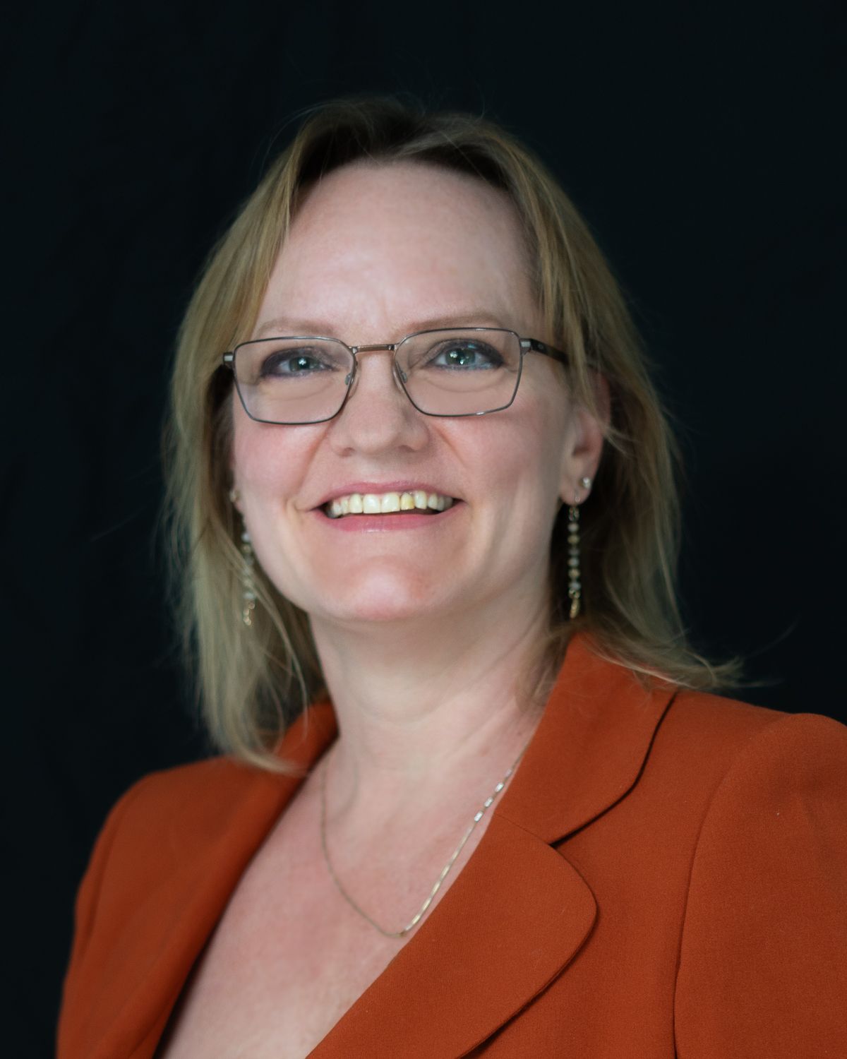 Executive portraits in rust-colored blazer against dark background showing confident poses.