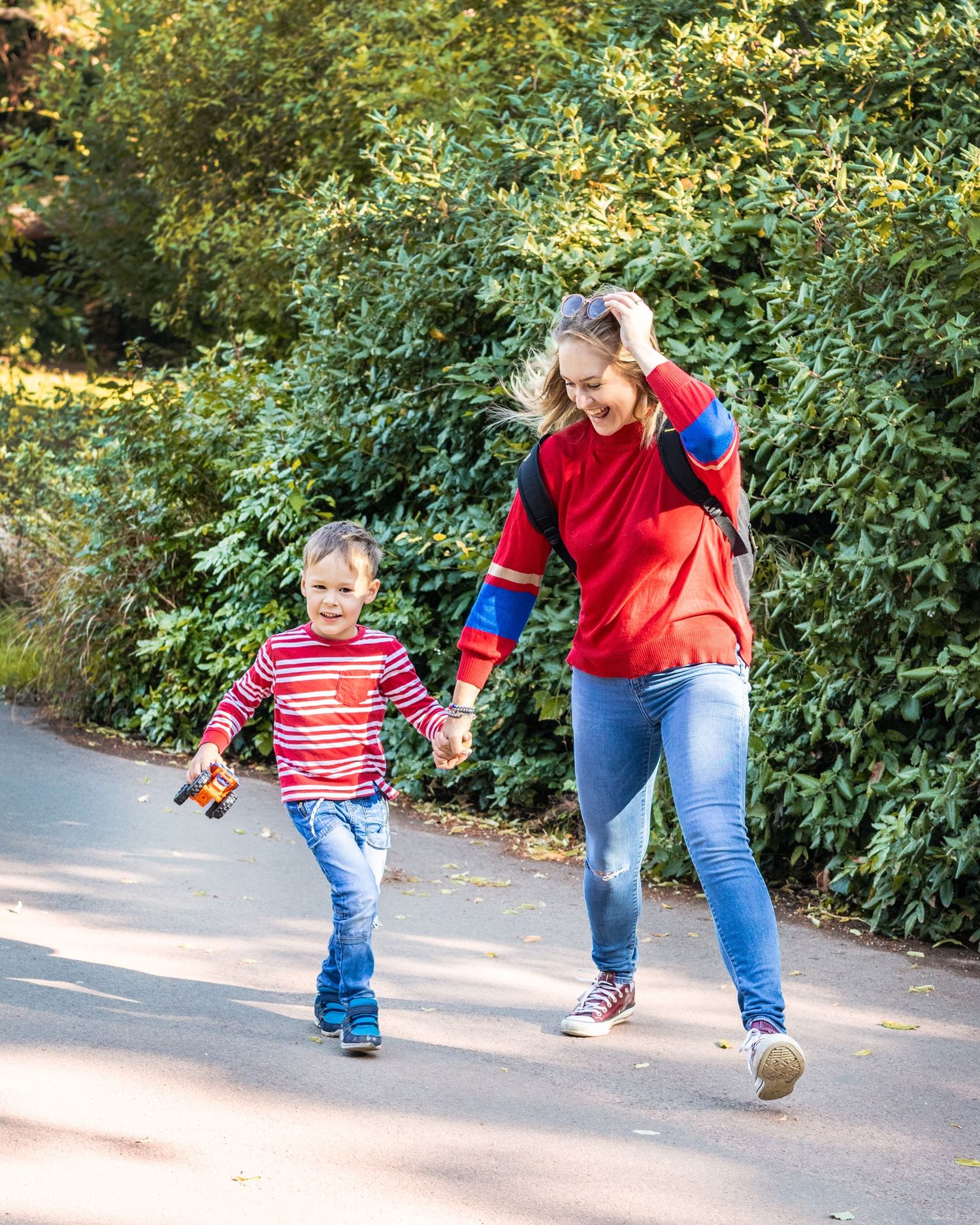 Parent and child holding hands while running together on a tree-lined path. Best female family photographer.