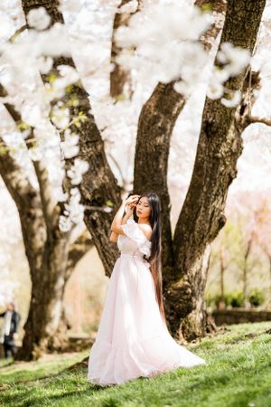 A flowing white wedding dress catches the spring breeze beneath blooming cherry trees in a dreamy garden setting.